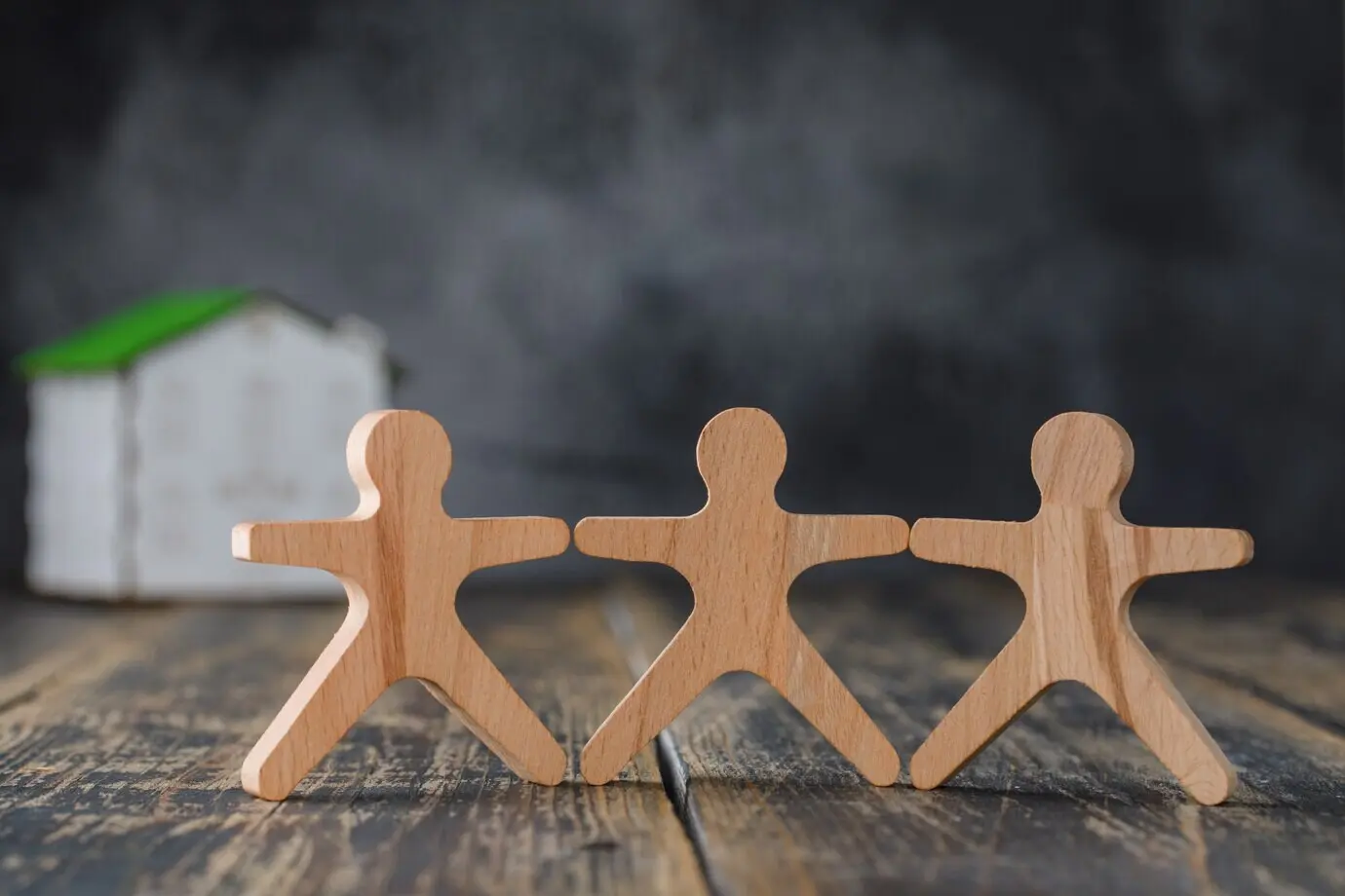 Concept of family safety depicted with wooden human figures and a side view of a model house.